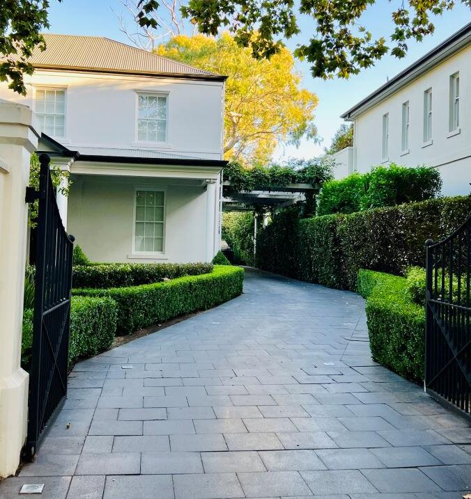 A Garden Managers horticulturist trims flowering shrubs, checks drip-line irrigation and inspects lush lawn growth—demonstrating end-to-end care in a single garden visit.